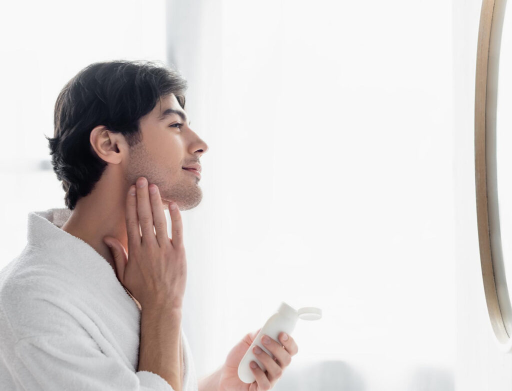 Image of a man in a white robe applying lotion to his vegan face. Vegan beauty products are becoming more common.
