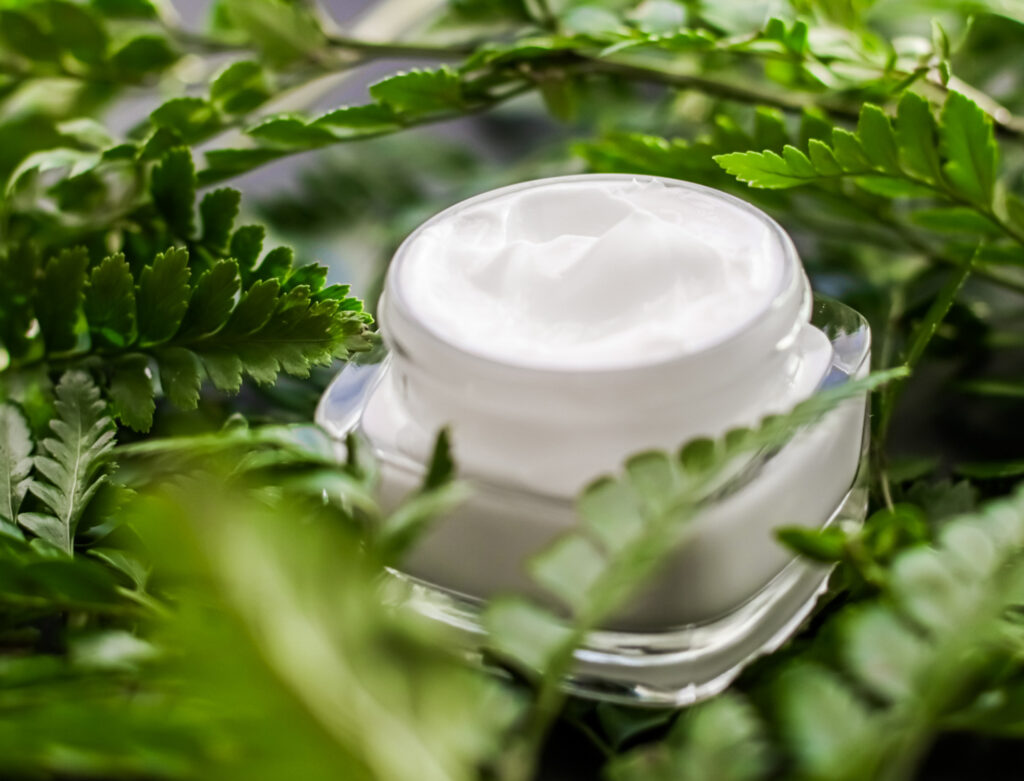 Image of a jar of lotion sitting amongst fern leaves. Cruelty-free labeling in the beauty industry can be deceiving.