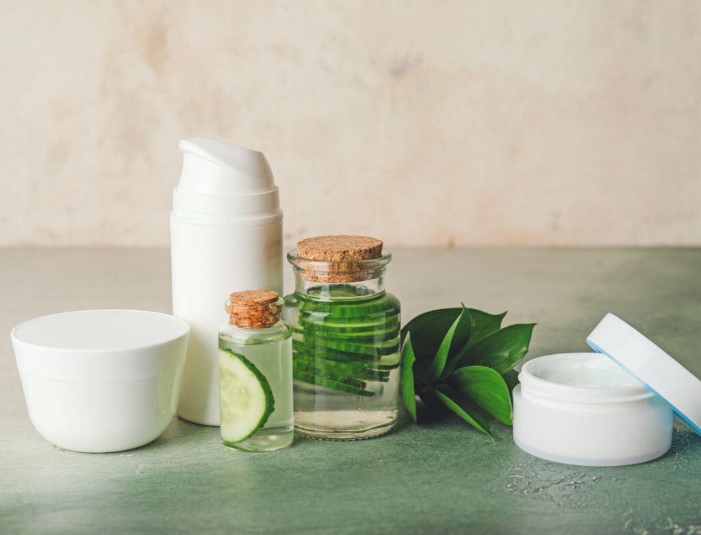 Image of vials and jars of lotions and oils on a green surface beside a leaf. Ethical production in the beauty industry takes animals, people, and the planet into consideration.