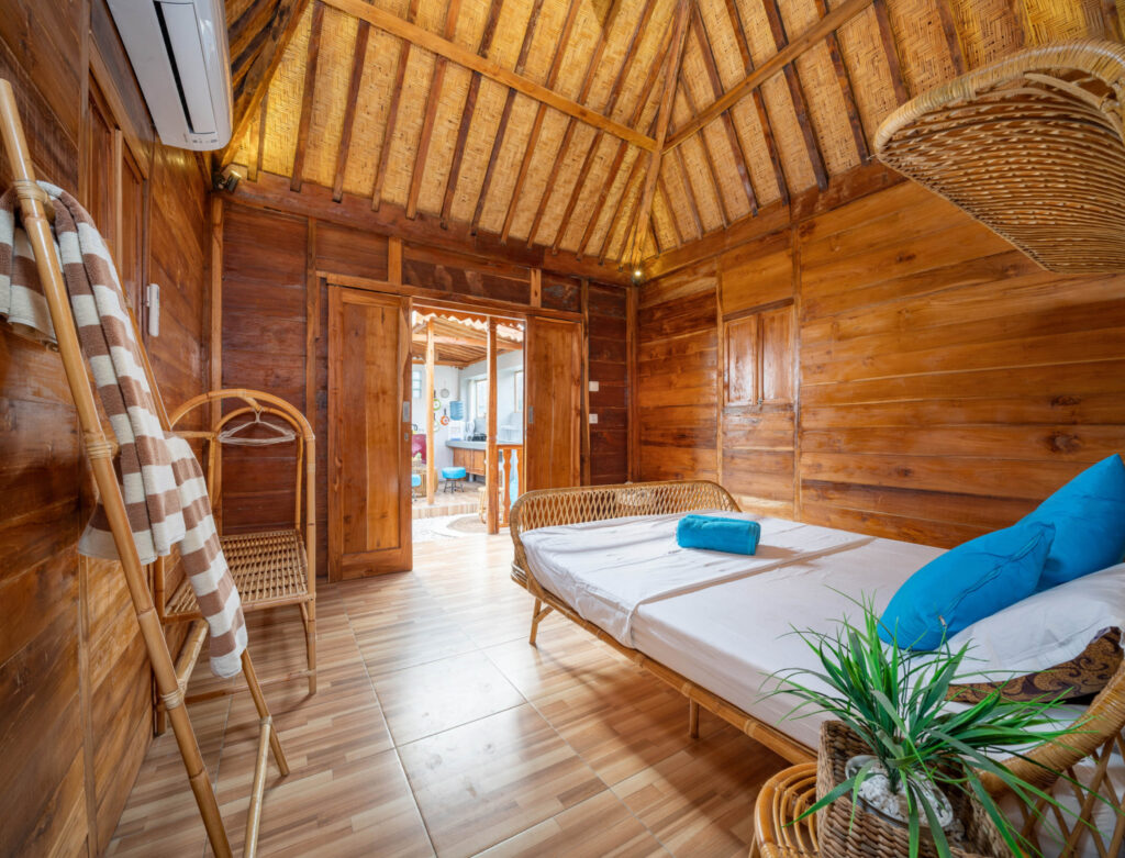 Image of the inside of a wooden structure with a bed, plant, and linens. Some sustainable eco-resorts offer individual cabins or huts on the beach!