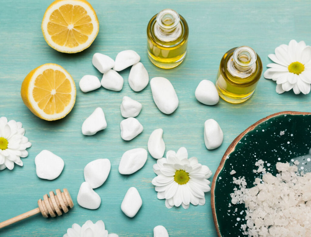 Image of natural ingredient for beauty product like lemon, honey, and essential oils on a blue surface taken from above. 