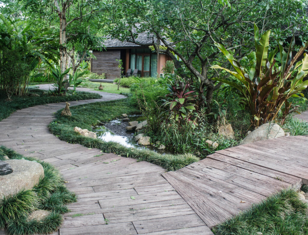 Image of a stone walkway surrounded by flora leading to a sustainable accommodation. Many eco-friendly vacation rentals offer privacy and peace for the soul.
