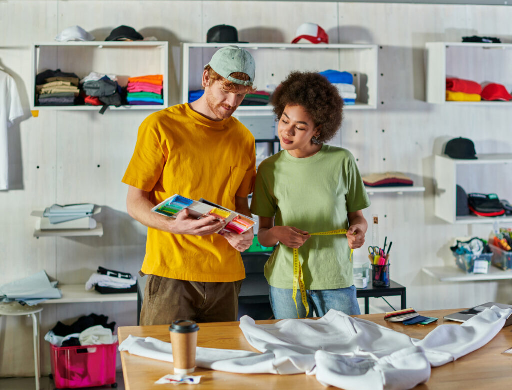 Image of two people standing at a workspace in a clothing shop. Utilizing sustainable materials like organic cotton is a good sustainable business example.
