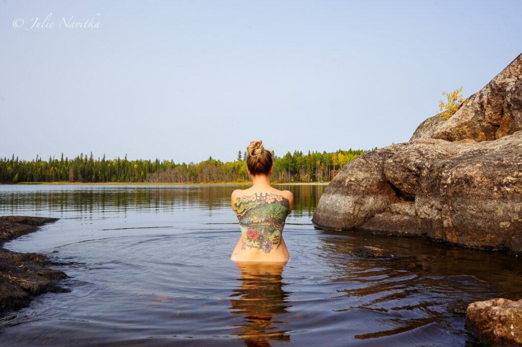 Image of a woman sitting in a lake near the shore, taken from behind. We must practice sustainable recreational swimming, meaning choosing eco-friendly spf. 