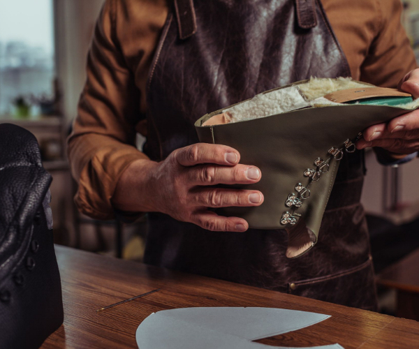 Image of a shoemaker's hands holding a grey boot that is halfway made. Many  sustainable european shoe brands are handcrafted.