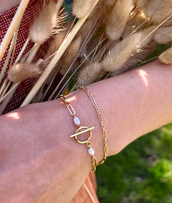 Image of a wrist wearing two delicate gold bracelets by Astor & Orion