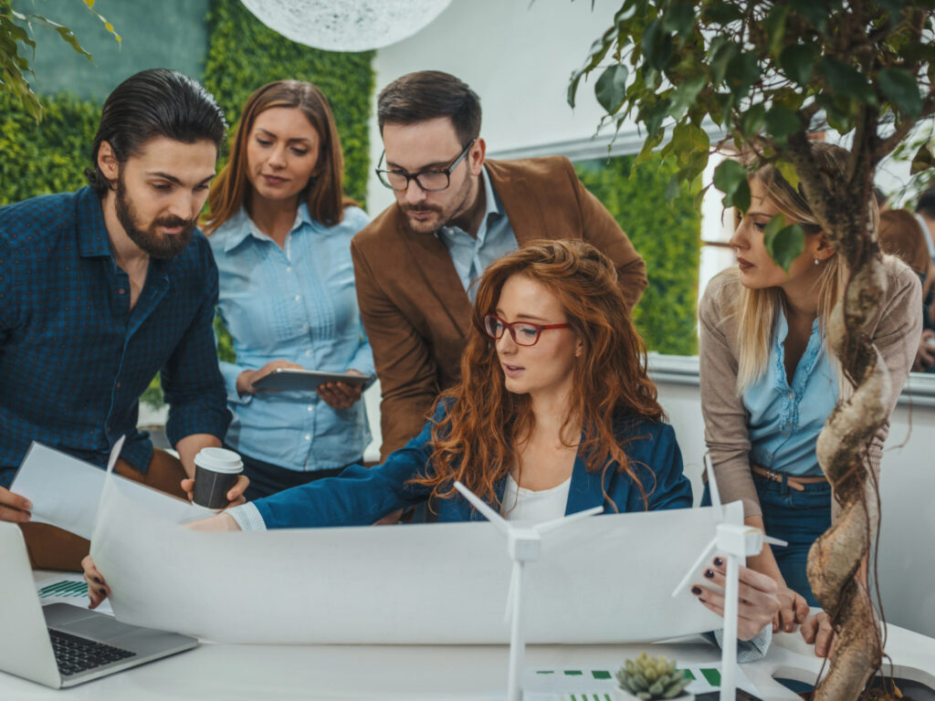Image of five coworkers looking at a project together in a green workspace.