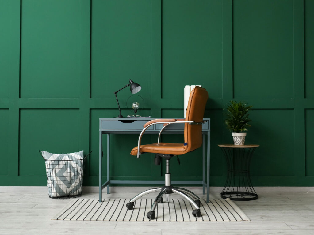 Image of a desk and chair home office set up against a dark green wall.