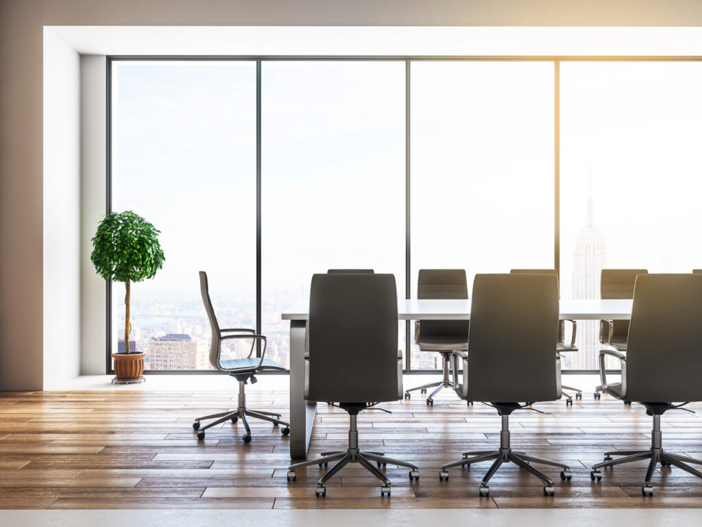 Image of a conference table in front of a floor to ceiling window bathing the room in sunlight. 