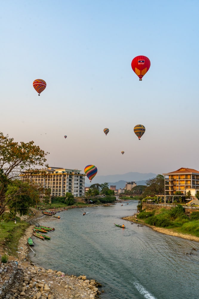 Image of many hot air balloons over the river. You can visit Vang Vieng sustainably by following the tips in this article. 