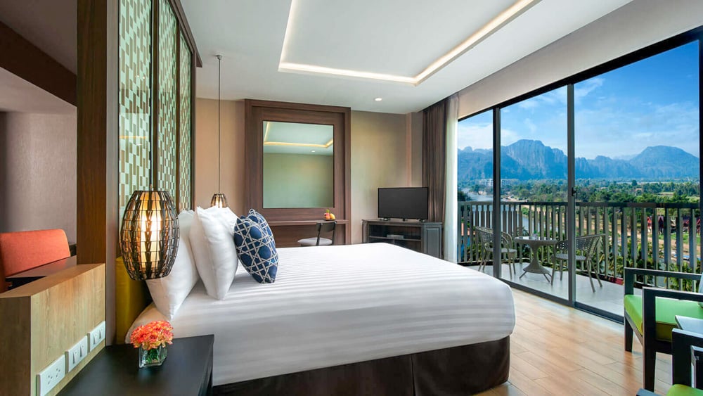 Image of a deluxe river view room with balcony at the Amari Vang Vieng, a lodging that prioritizes sustainability.