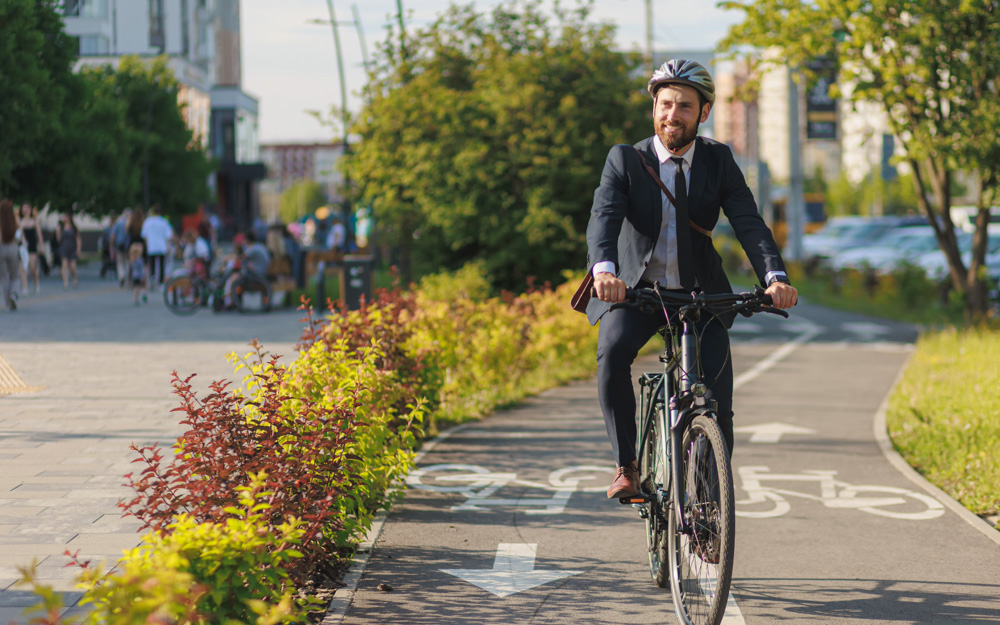 A man in a suit rides his bike to work on a bike path on a nice spring day. Make sustainable transport part of your climate-friendly routine this spring!