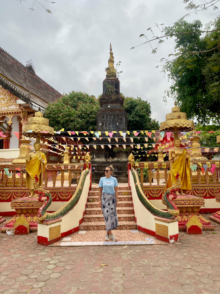 Image of a woman standing in front of a pagoda in Vang Vieng, Laos. Visit Vang Vieng sustainably by respecting dress codes in sacred places. 