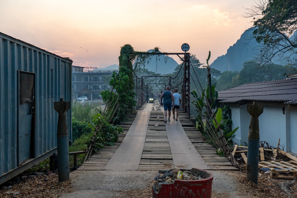 Image of an old bridge taken from one end at dusk as a couple walks across, away from the camera. 