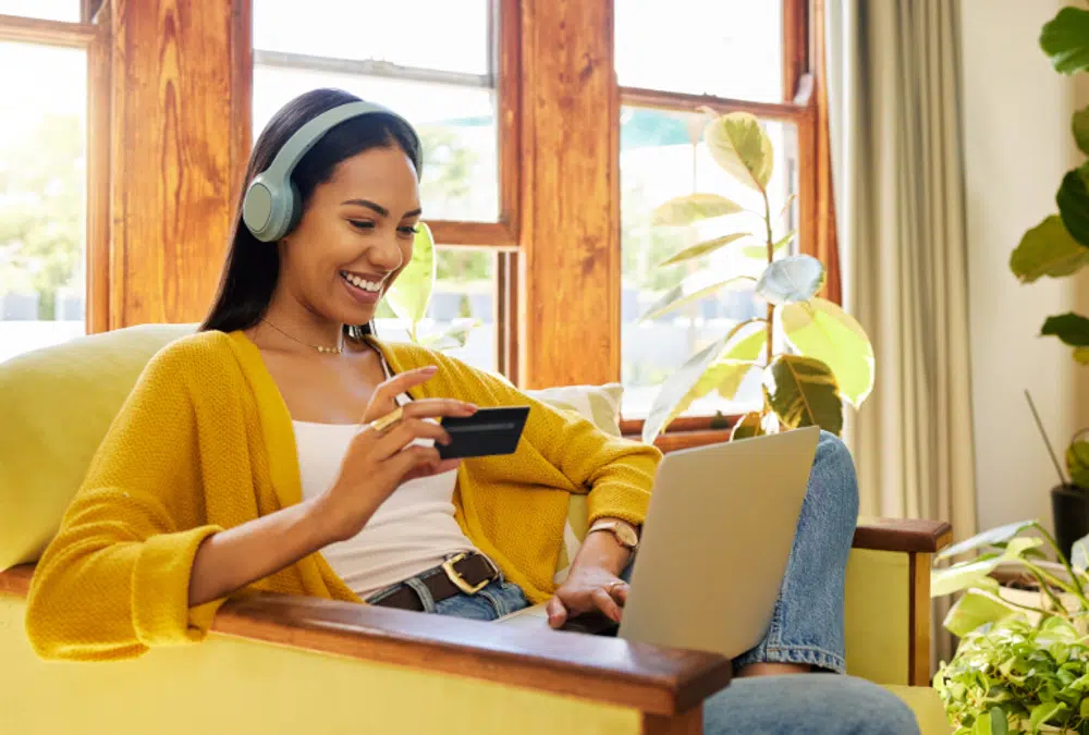 Image of a woman sitting on a couch with her laptop and credit card in hand, visiting a secondhand shopping platform.