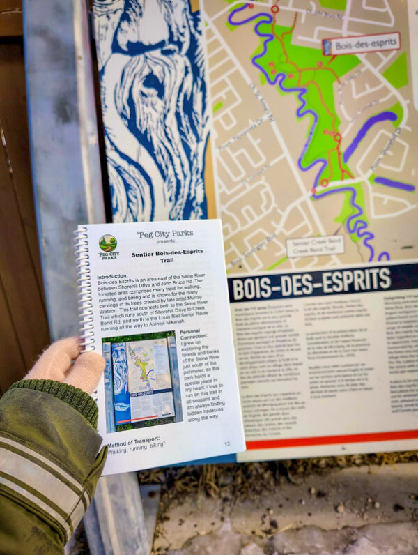 Image of the 'Peg City Parks - Explore Winnipeg's Green Spaces" book in front of the Bois-des-Esprits trail sign, featuring scavenger hunts for 10 different Winnipeg parks.