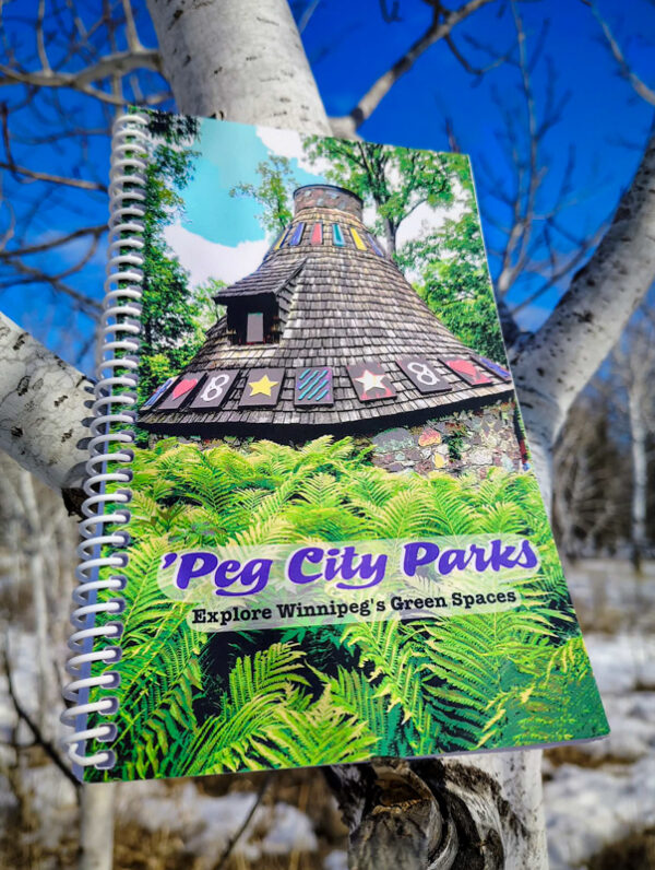 Image of the 'Peg City Parks - Explore Winnipeg's Green Spaces" book in a tree, featuring scavenger hunts for 10 different Winnipeg parks.