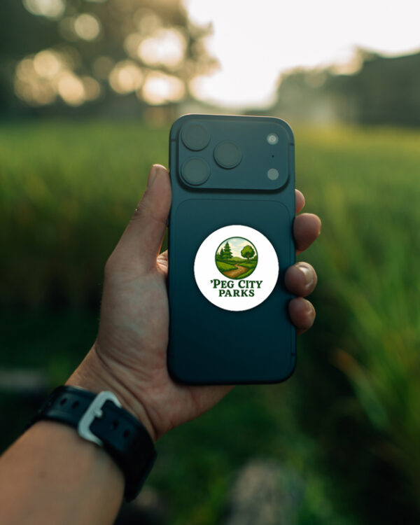 Image of the Peg City Parks circular glossy sticker on a smartphone.